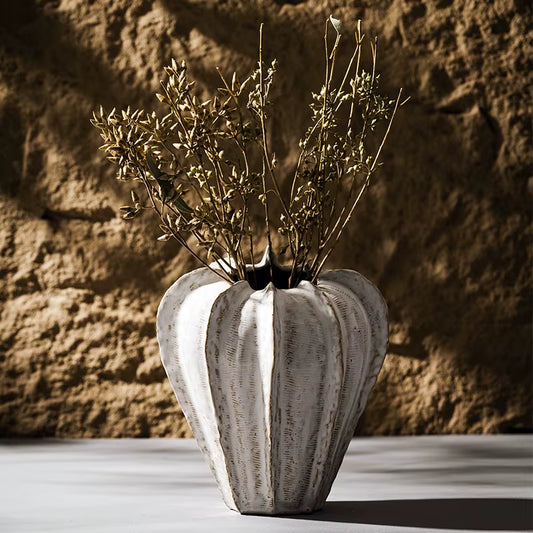 Tall ribbed ceramic pod vase holding dried stems.