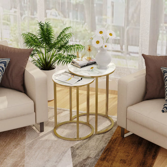 Nesting side tables with white tops and gold frames between two armchairs in a living room.