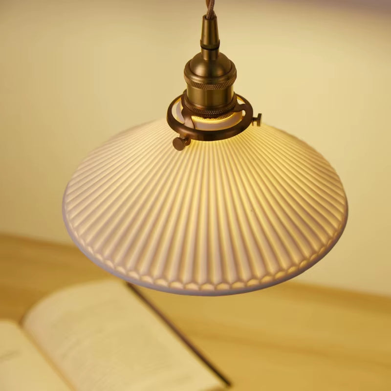 Close view of the white pleated pendant shade, lit, seen from the side.