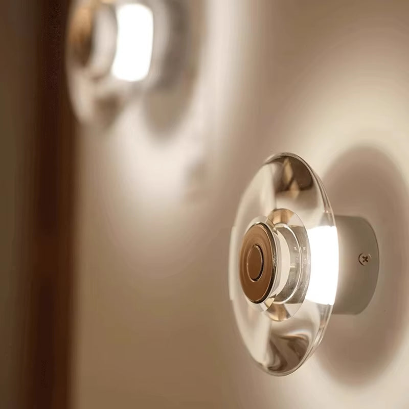 Close view of the clear crystal disc wall sconce, lit, on a warm-toned wall.