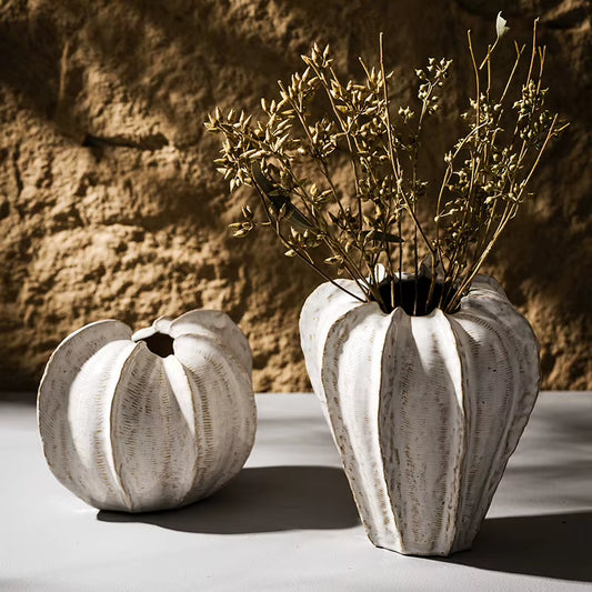 Two ribbed ceramic pod vases in antique white, the tall pod holding dried stems beside the round pod.