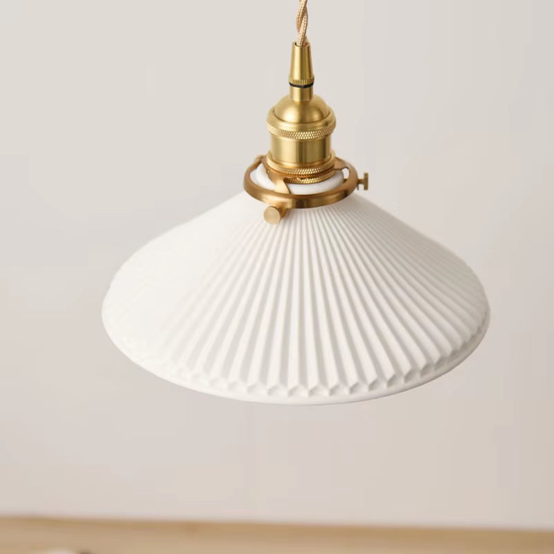 Close view of the white pleated shade and copper-finish holder of the pendant light, unlit.
