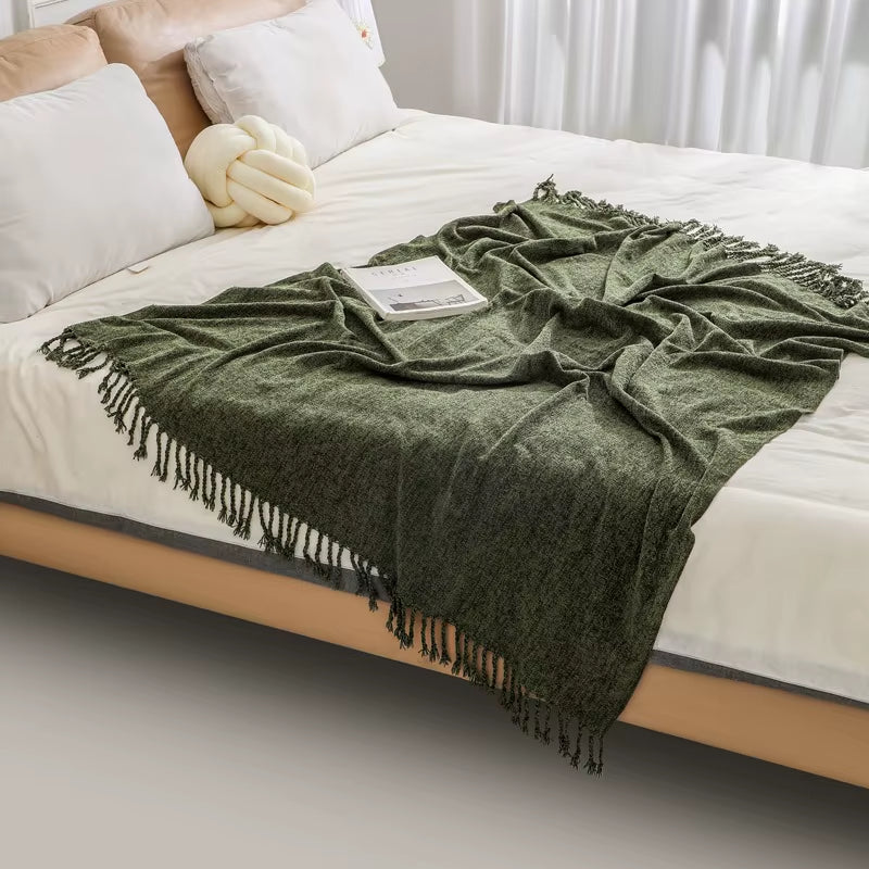 Army green chenille throw blanket with fringe spread across the foot of a bed.