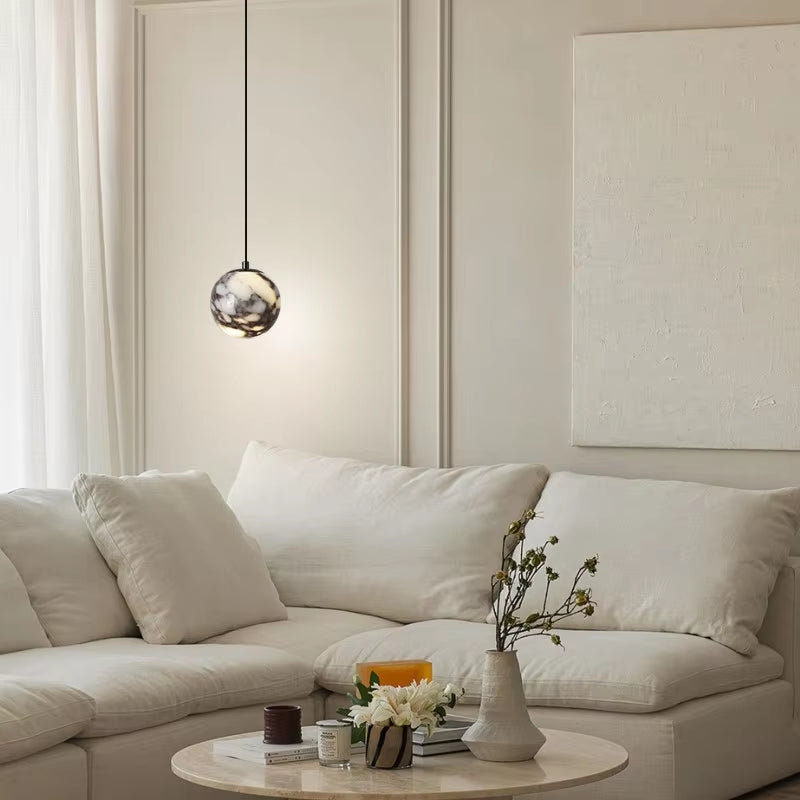 Marble globe pendant light, lit, hanging beside a white sofa in a living room.