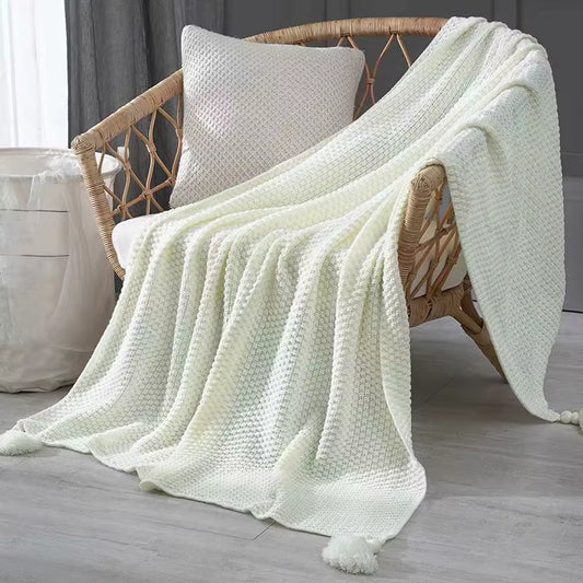 Cream white waffle knit throw with tassels draped over a rattan chair.