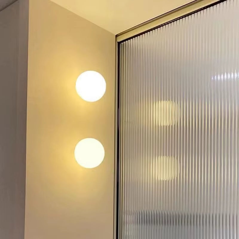Two frosted glass globe wall lights, lit, beside a fluted glass partition.
