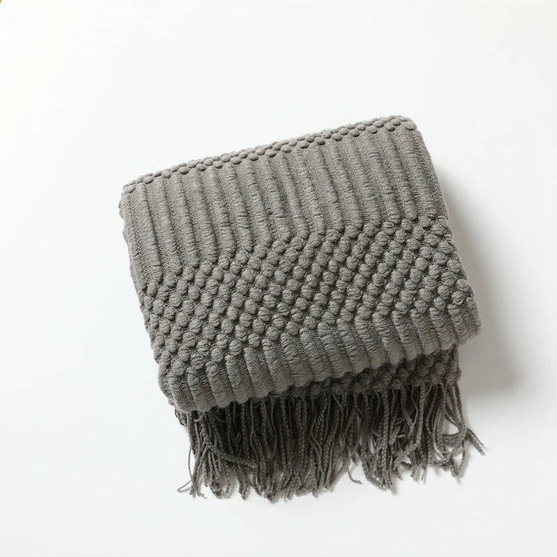 Folded dark grey chunky knit throw with a textured band and tassels.