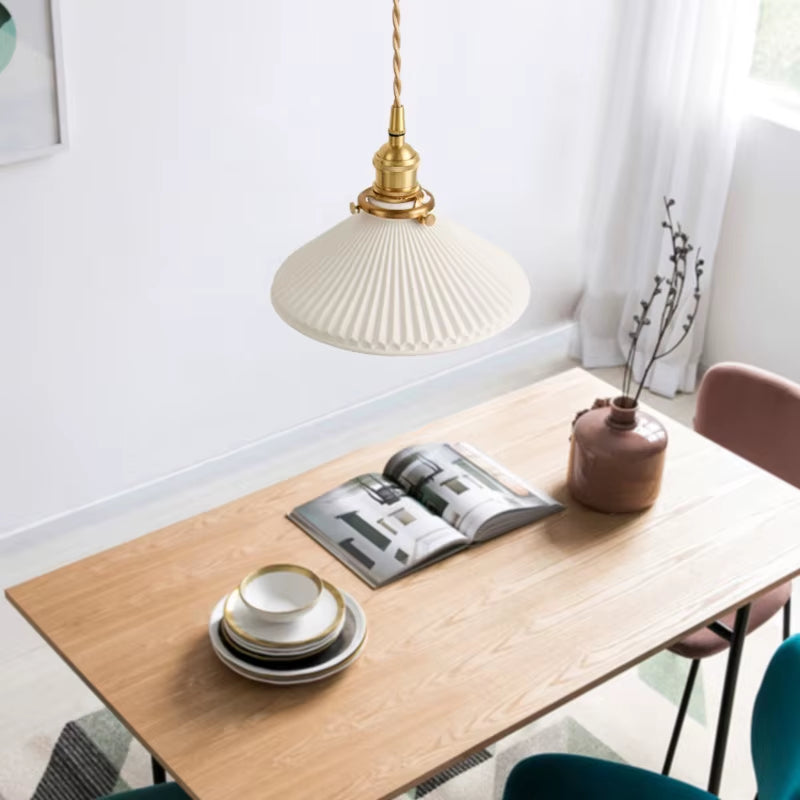 White pleated pendant light hanging above a wood dining table.