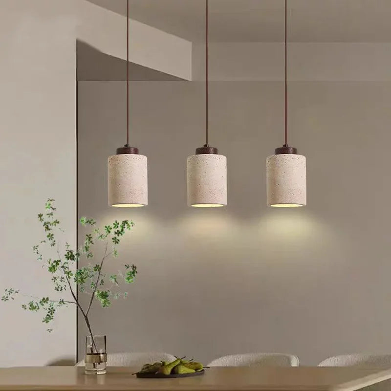 Three tall travertine cylinder pendant lights hanging over a table.