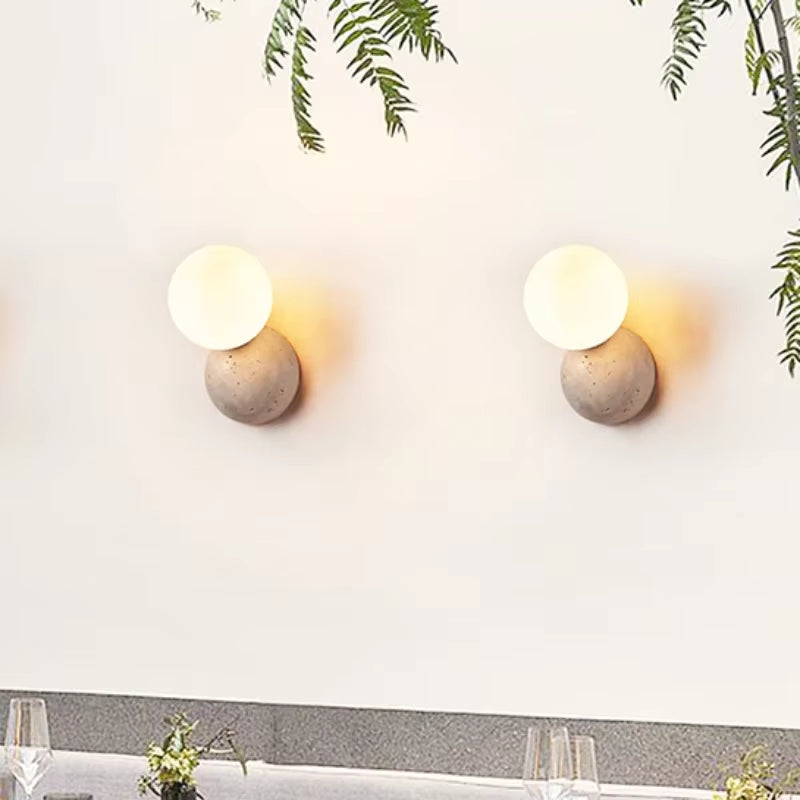 Two stone dome wall sconces with frosted glass globes on a wall above a dining table.