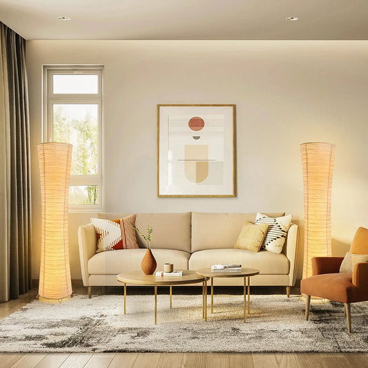Rice paper column floor lamps lit on both sides of a cream sofa in a bright living room.