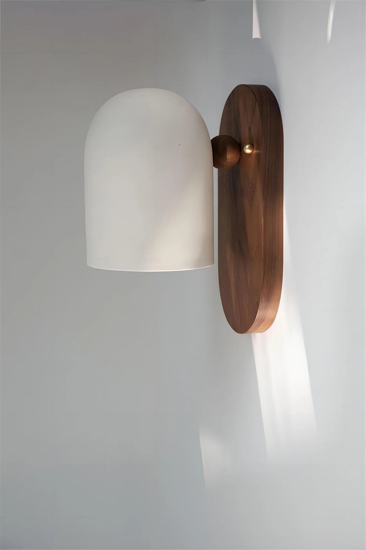 Oblong backplate wall sconce with a white bell shade on a wall in daylight