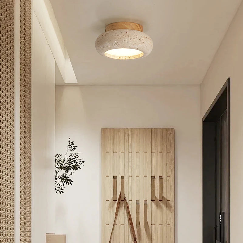 Rounded travertine ceiling light with a light wood canopy lit in an entryway