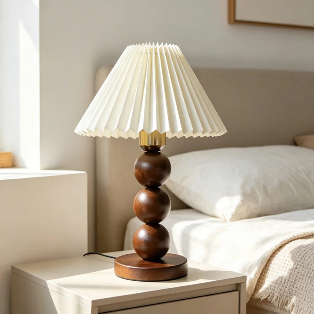 Walnut-color stacked-sphere table lamp with a white pleated shade on a white nightstand.