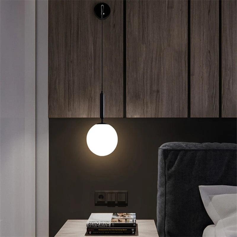 Frosted globe wall sconce on a black metal drop arm, lit, on a dark wood wall above a nightstand.