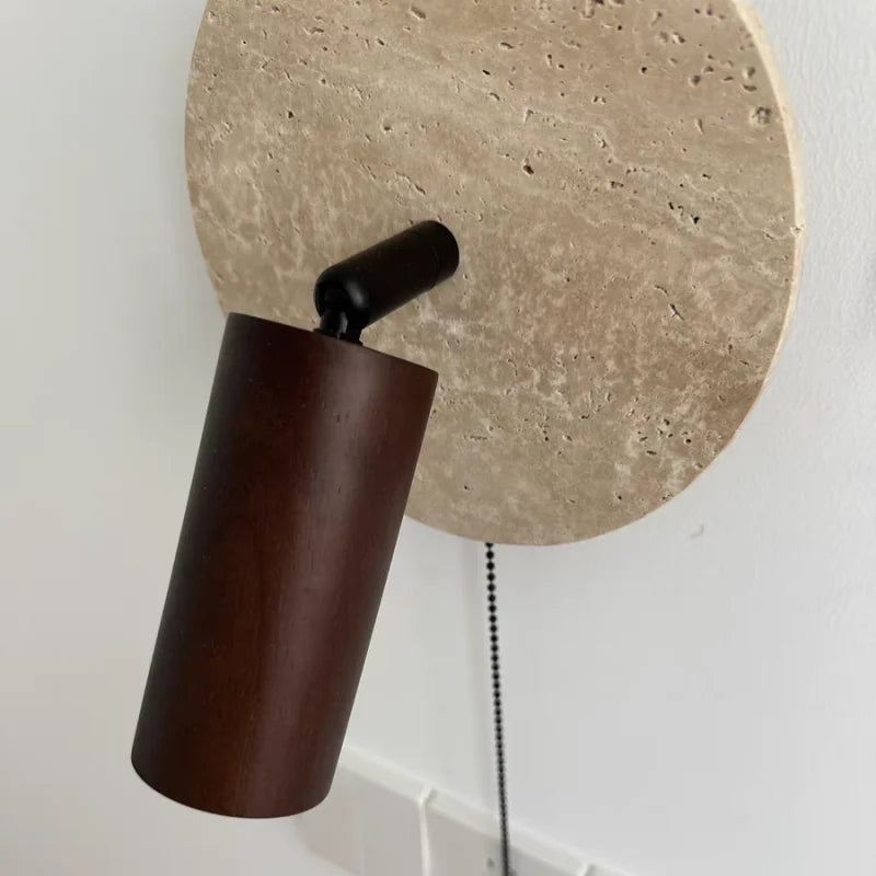 Close view of the dark wood spotlight, the travertine disc and the pull chain