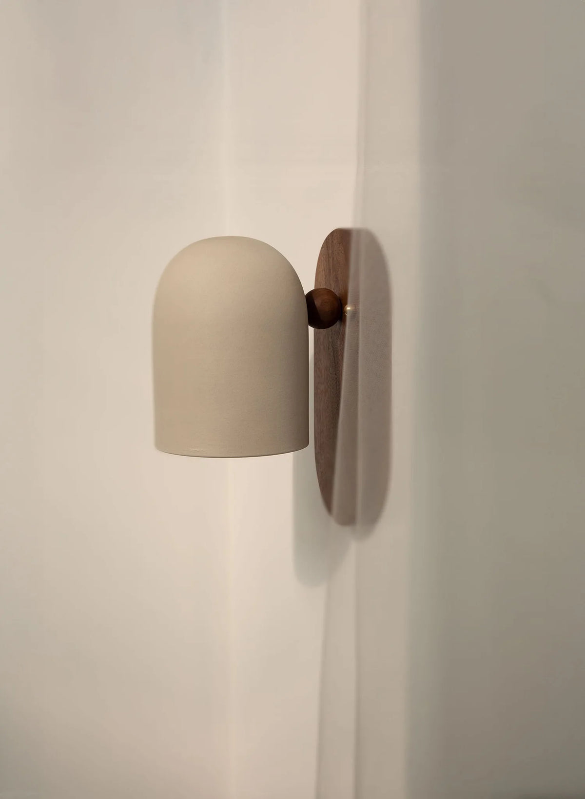 Oblong backplate wall sconce with a white bell shade on a beige wall