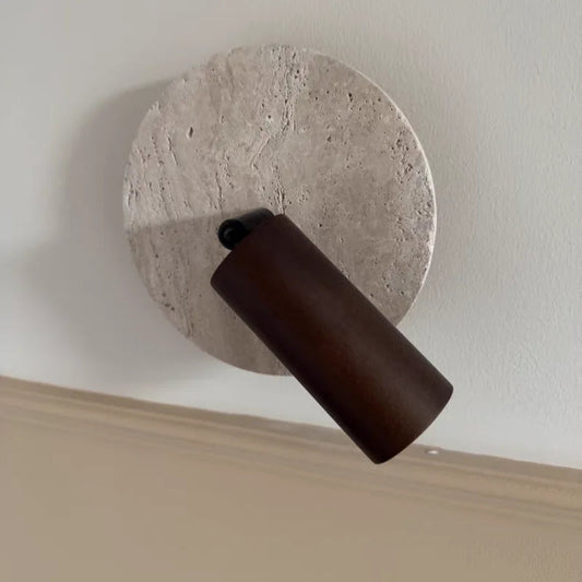 Travertine disc wall sconce with a dark wood spotlight angled down