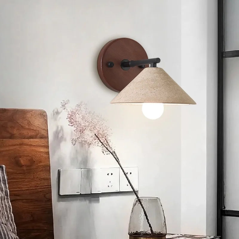 Travertine cone wall sconce lit beside a headboard