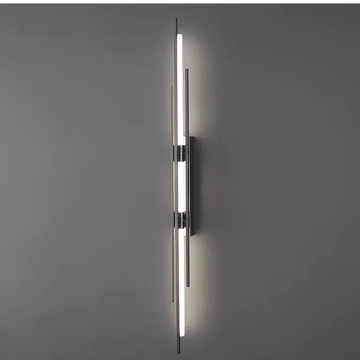 Linear black wall sconce lit on a plain gray wall, front view