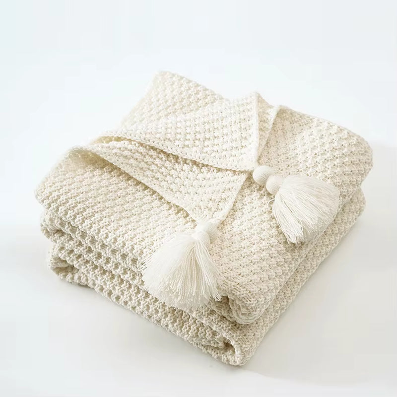 Folded beige waffle knit throw with corner tassels.