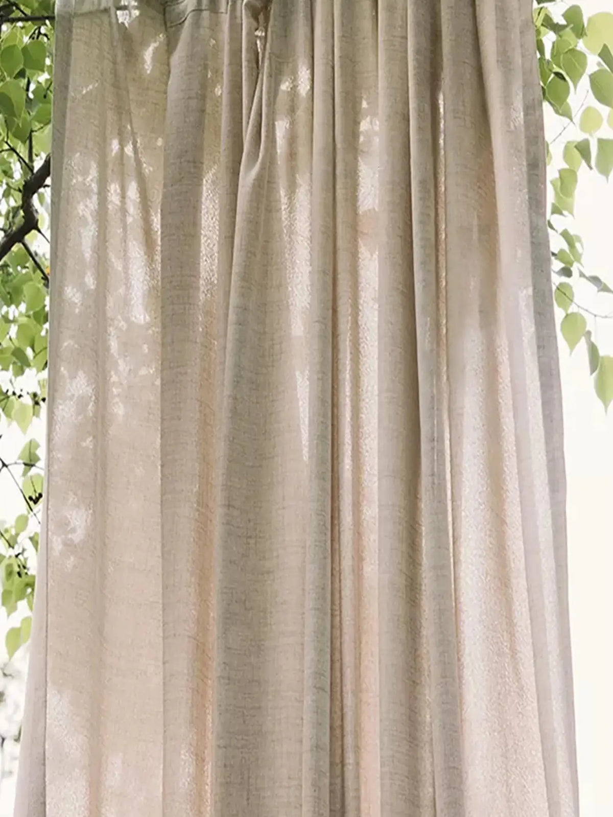 Natural beige semi-sheer curtain panel with greenery visible behind it.