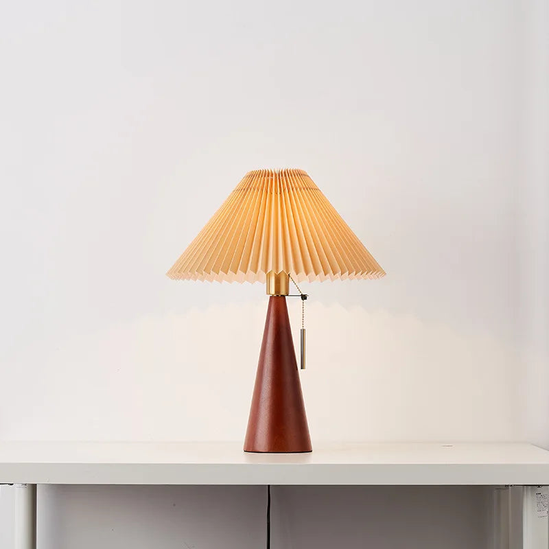 Walnut wood cone table lamp with a pleated fabric shade, lit.