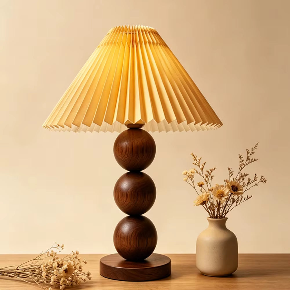 Walnut-color stacked-sphere table lamp with a walnut-toned pleated shade beside a vase of dried flowers.