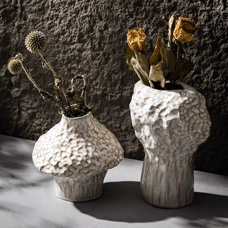 Two matte white ceramic vases with a hammered texture, short and tall, holding dried flowers.