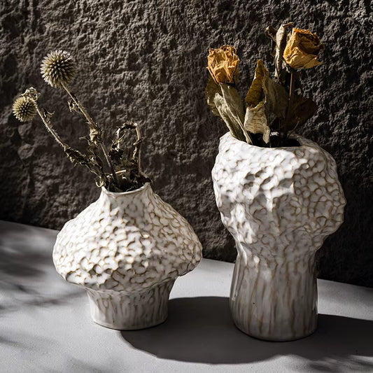 Two matte white ceramic vases with a hammered texture, short and tall, holding dried flowers.