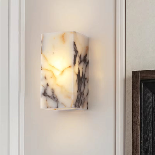 Stone block wall sconce, lit, on a panelled wall beside a dark wood door frame.