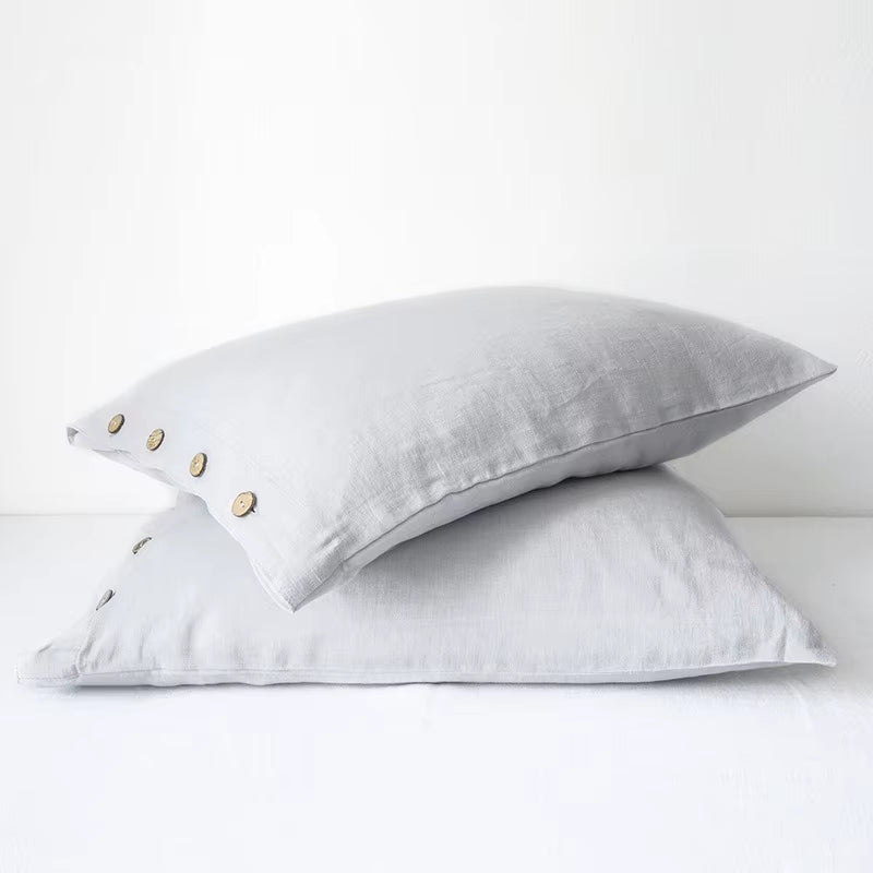 Two light grey linen pillow covers with button closures, stacked.
