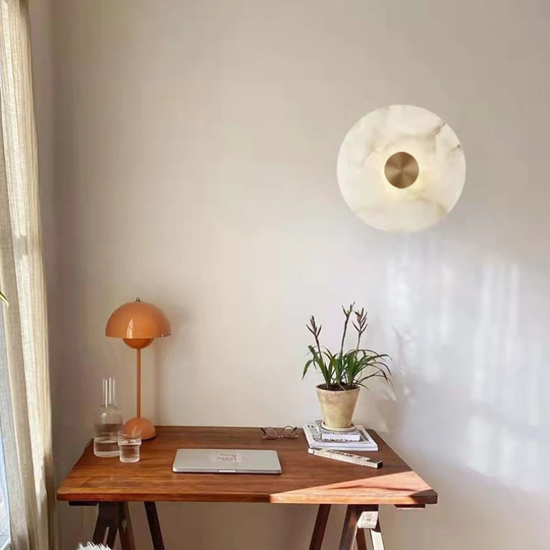 Round marble disc wall sconce with a metal center on a wall above a wood desk.