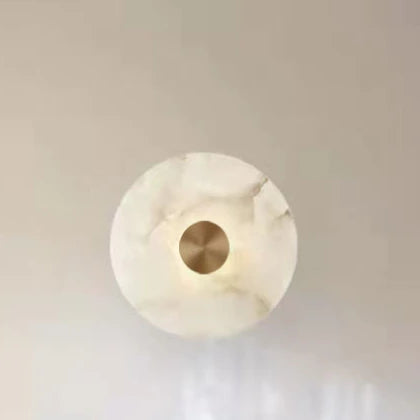 Round marble disc wall sconce with a metal center on a pale wall.