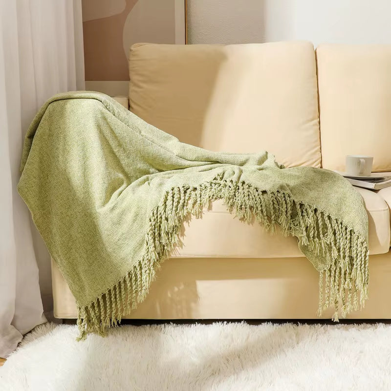 Matcha green chenille throw blanket draped over the arm of a cream sofa.