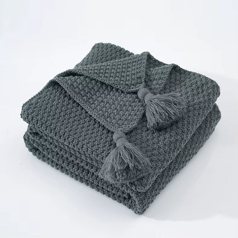 Folded gray waffle knit throw with corner tassels.