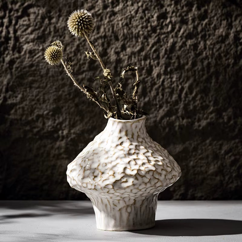 Short hammered ceramic vase in matte white holding dried thistle stems.