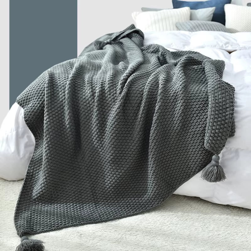 Gray waffle knit throw with tassels on a bed.