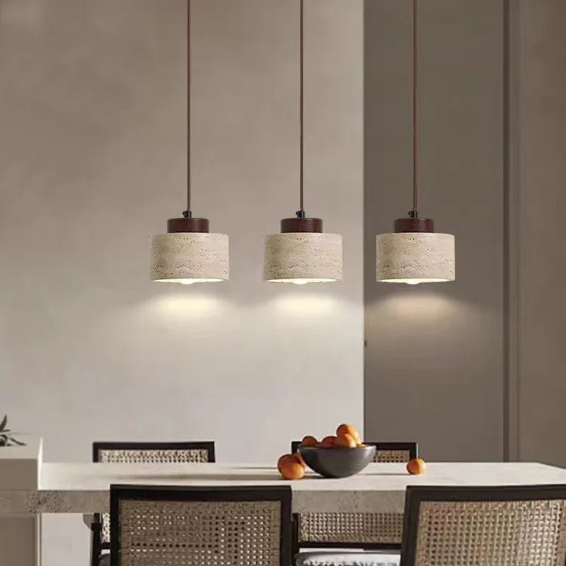Three short travertine cylinder pendant lights hanging over a dining table.