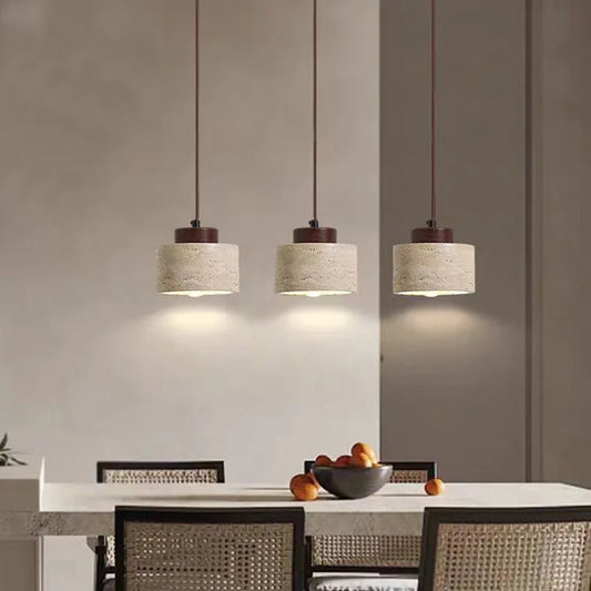 Three short travertine cylinder pendant lights hanging over a dining table.