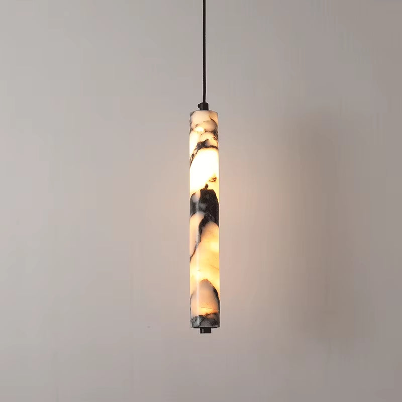 Slim marble cylinder pendant light on a black cord, lit, against a gray wall.