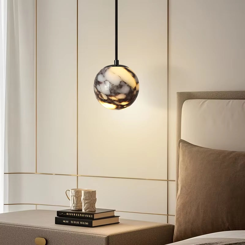 Marble globe pendant light, lit, hanging above a nightstand beside a bed.