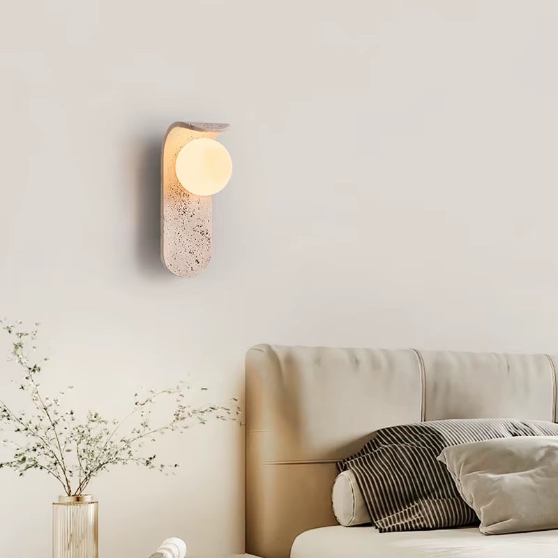 Travertine globe wall sconce lit on a wall above a sofa