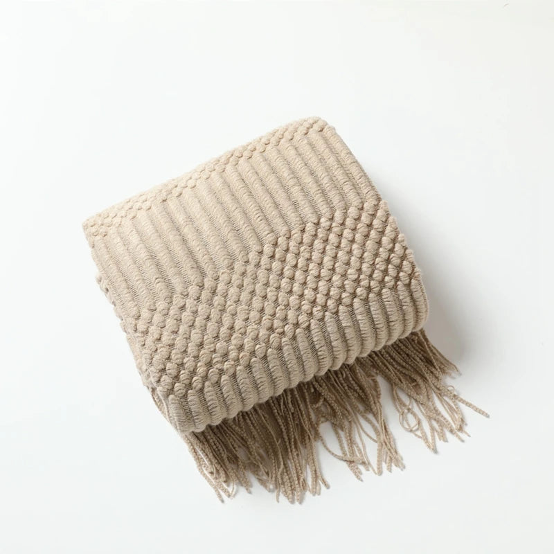 Folded khaki chunky knit throw with a textured band and tassels.