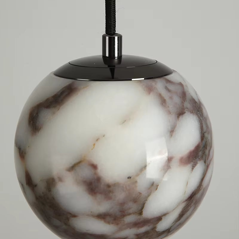 Close view of the marble globe pendant, unlit, showing the dark metal cap and the veining.