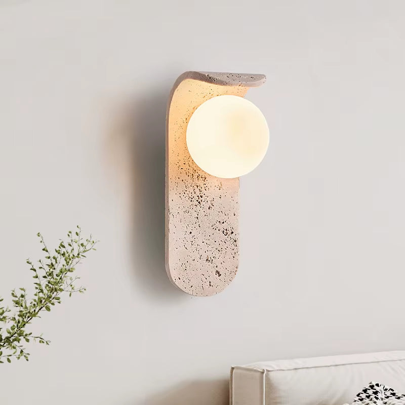 Travertine globe wall sconce lit on a plain wall, seen at an angle