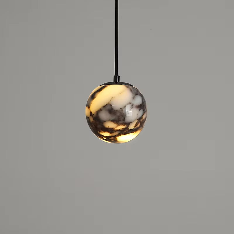Marble globe pendant light on a black cord, lit, against a gray wall.