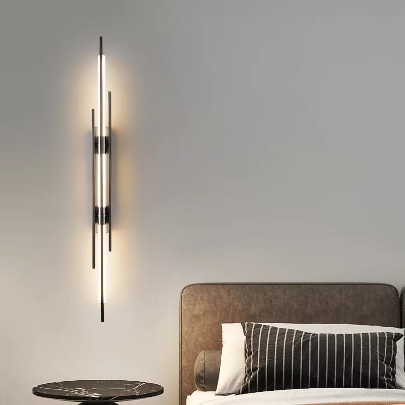 Linear black wall sconce lit beside a bed