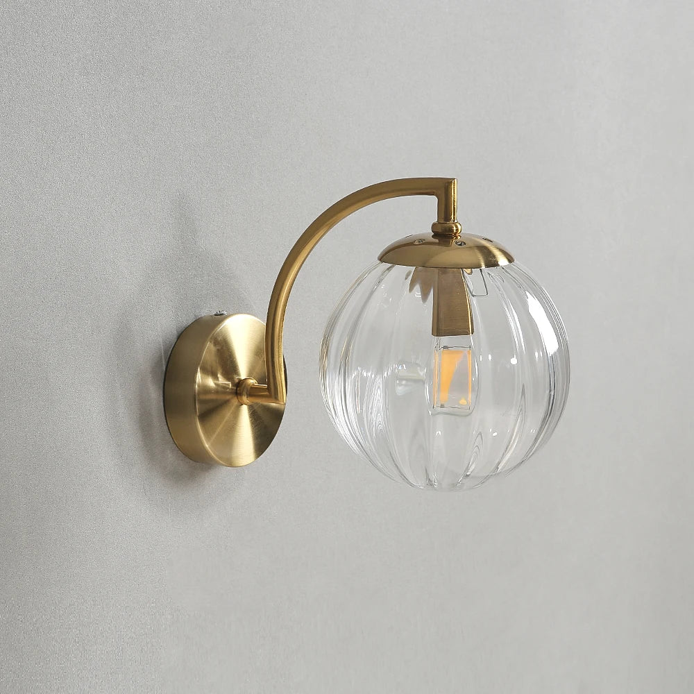 Glass wall sconce with a clear ribbed glass globe on a gold-color curved arm, unlit.