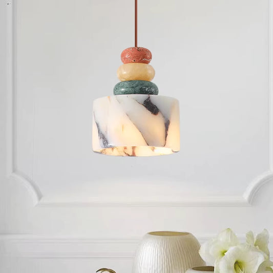 Natural stone drum pendant light under three stacked stone discs, lit, in front of a panelled wall.